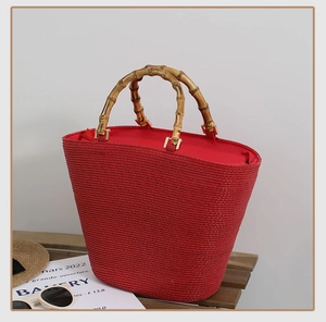 Close-up of red straw tote bag featuring natural bamboo handles and gold metal hardware