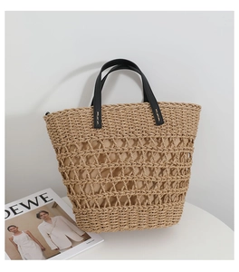 Detail of hollow woven straw tote bag with fabric liner and black leather handles
