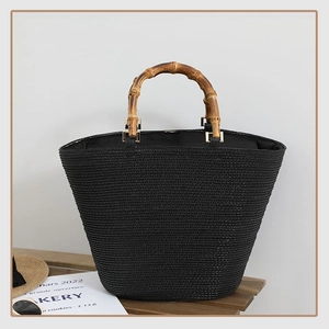 Close-up of black woven tote bag featuring natural bamboo handles and gold metal hardware