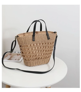Detail of hollow woven straw tote bag with black handles and adjustable shoulder strap