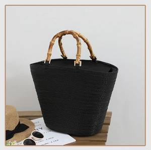 Detail of black straw tote bag featuring natural bamboo handles and gold metal hardware