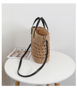 Detail of hollow woven straw tote bag with black leather straps and beige inner lining