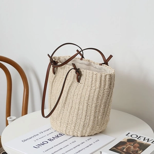 Minimalist cream straw woven tote bag with brown leather handles on a white table