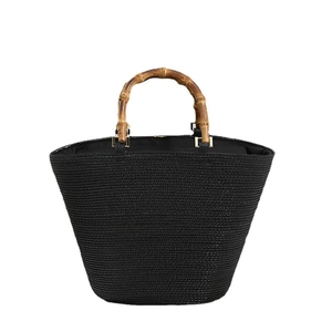 Large black woven straw tote bag with natural bamboo top handles and gold metal rings