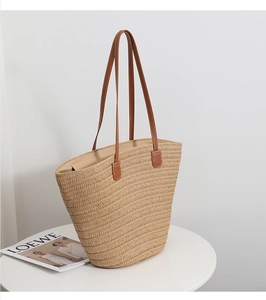 Detail of straw tote bag showing woven texture, brown leather handles, and zipper closure