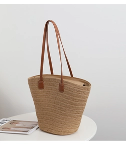 Detailed view of natural straw woven tote bag with premium brown leather handles and stitching