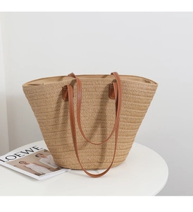 Close-up of a woven straw tote bag with brown leather straps on a white tabletop