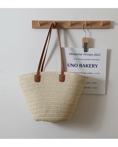 Detailed close-up of straw tote bag with brown leather handles hanging on a wooden hook