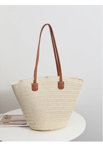 Detailed texture of hand-woven straw tote bag with brown leather handles on a white table