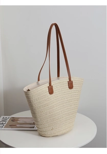 Detail of the woven texture and brown leather handle on a large straw tote bag