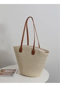Detail of minimalist straw tote bag with brown faux leather handles on a white table