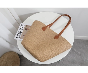 Detailed shot of straw tote bag featuring brown leather straps and contrast stitching