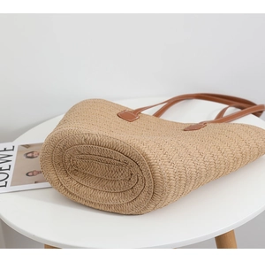 Detailed view of woven straw tote bag bottom with reinforced texture and leather handle