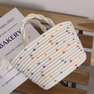 Handmade woven handbag with colorful pom-poms and twisted cotton handles on a chair