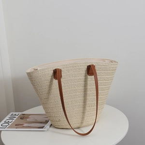 Large straw tote bag with brown leather handles on a white table for beach vacations