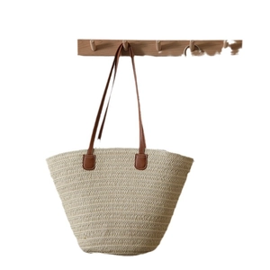 Minimalist beige woven straw tote bag with brown leather handles for beach vacation
