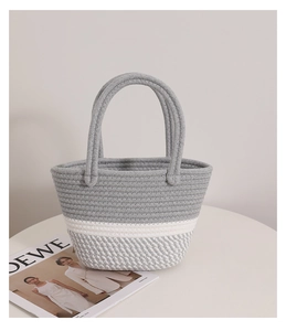 Close-up of grey and white woven cotton rope bag on white table with fashion magazine