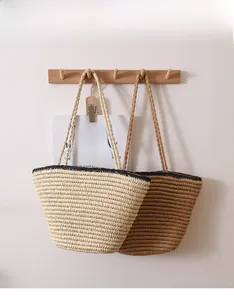 Detail of hand-woven straw bags with black trim hanging on a wooden rack for summer