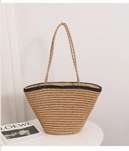 Detail of hand-woven straw tote with black contrast trim on a white minimalist table