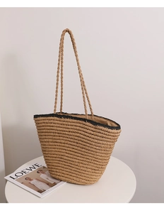 Detail of hand-woven straw tote with black contrast trim and fine texture on a white table