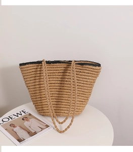 Detail view of woven straw tote bag with black trim and long handles on white table