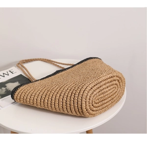 Detail of woven straw tote bag with black trim and spiral thick base on white table