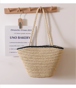 Detail of hand-woven straw tote with black contrast trim hanging on a wooden hook