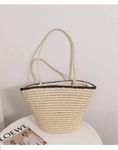 Detail view of woven straw tote bag with black contrast trim on a minimal white table
