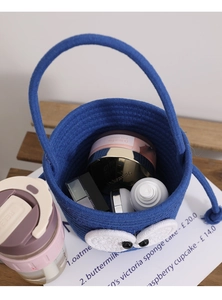 Blue cotton rope woven bucket bag featuring large cartoon eyes and cosmetic items inside