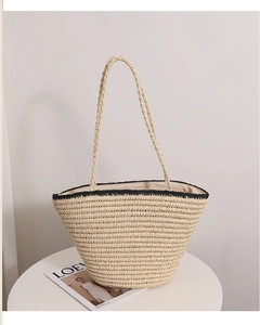 Detail of beige straw tote bag with black woven trim and long handles on white table