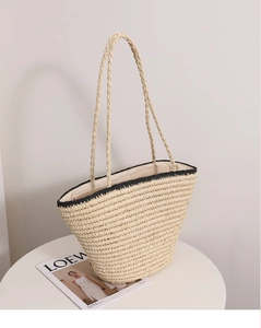 Detailed close-up of woven straw tote with black contrast trim on a display stand