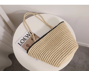 Close-up of woven straw tote bag with black trim and long knot handles on a table