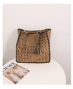 Dettaglio borsa tote in paglia con bordo nero a contrasto e nappa su tavolo bianco