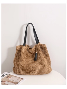 Detail of hand-woven straw tote with black leather straps and decorative fringe tassel