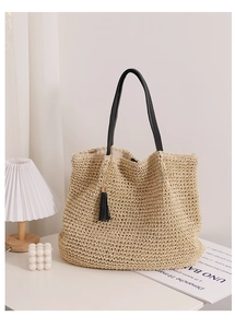 Detail of woven straw tote bag with black leather handles and elegant tassel ornament