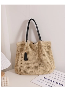 Detail of the woven straw tote bag featuring black leather handles and fringe tassel charm