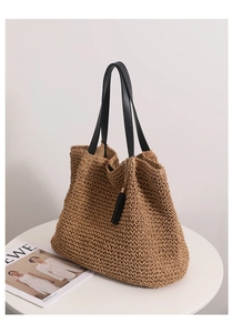 Close-up of woven straw tote bag featuring black leather handles and tassel detail
