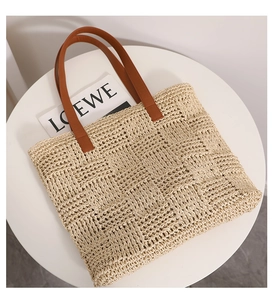 Detail of checkered woven straw tote bag with brown leather handles on a white table