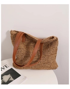 Detailed close-up of handmade straw tote bag with brown leather straps and woven texture