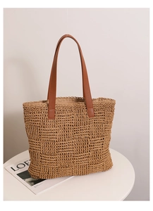 Detail of checkered woven straw tote bag featuring brown faux leather handles on a table