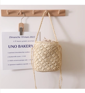 Detail of a beige woven bucket bag hanging on a wooden hook against a cream wall