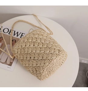 Detail of hollow geometric woven straw bag with golden metal rings and beige strap