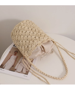 Close-up of beige woven straw bucket bag with internal drawstring pouch and hollow texture