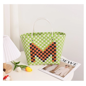 Detail of green and white woven tote bag with orange M letter and clear handles