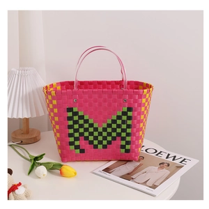 Detail of pink and yellow woven basket bag featuring green M letter and clear handles