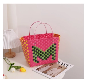 Detail of woven tote bag with green letter M, transparent handles and rivet accents