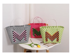 Close-up of three woven tote bags in contrasting colors with M logo and clear handles