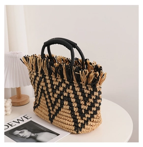 Detail of checkered woven straw tote bag with black round handles and fringed edges