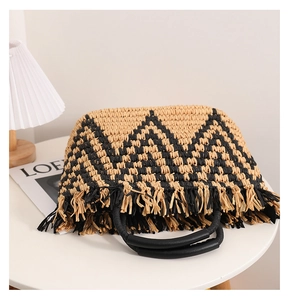 Detail of bohemian straw handbag featuring black geometric weave and fringed edges