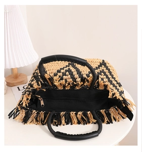 Detail of checkerboard straw bag with long fringe edges and black leather handles